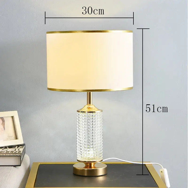 Elegant gold-toned table lamp with decorbites clear crystal faceted glass base and cream fabric shade for bedroom decor
