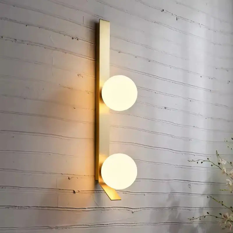 Gold-toned wall lamp with two frosted glass ball nordic shades on a sleek vertical bar for living room decorbites