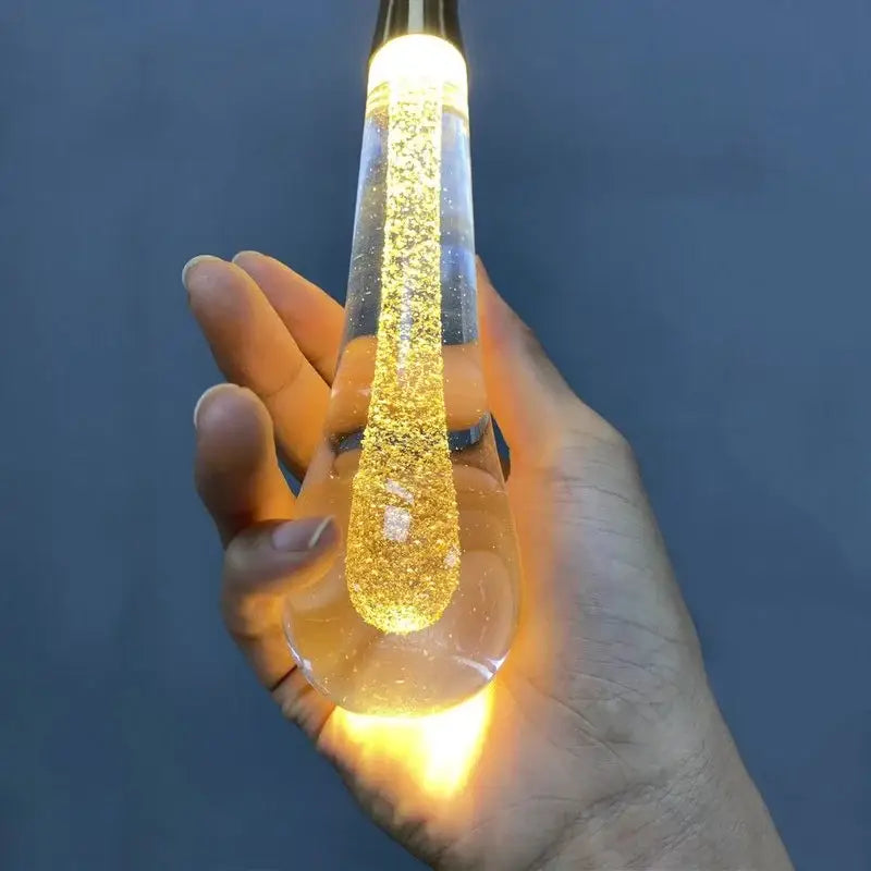 A glowing gold liquid crystal drop pendant light with transparent glass and glittery swirling decorbites crystal drop design