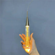 A gold liquid crystal drop pendant light with clear glass filled with golden glitter and a sleek gold metal cap for decorbites crystal drop decor