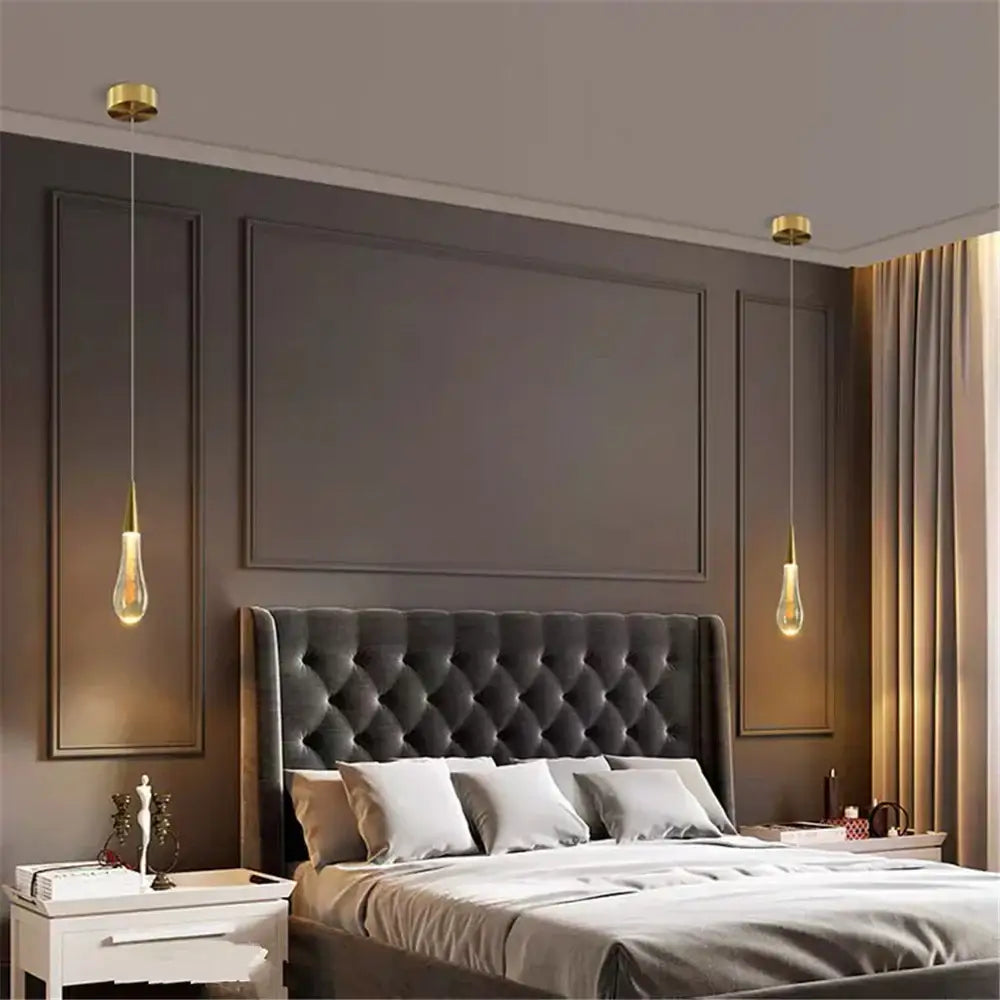 Two elegant gold-toned decorbites crystal drop pendant lights with teardrop glass shades hang above a tufted bed