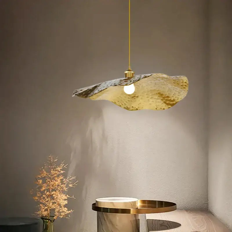 A modern hammered gold pendant light with an organic lotus leaf shape for decorbites gold lotus living room decor