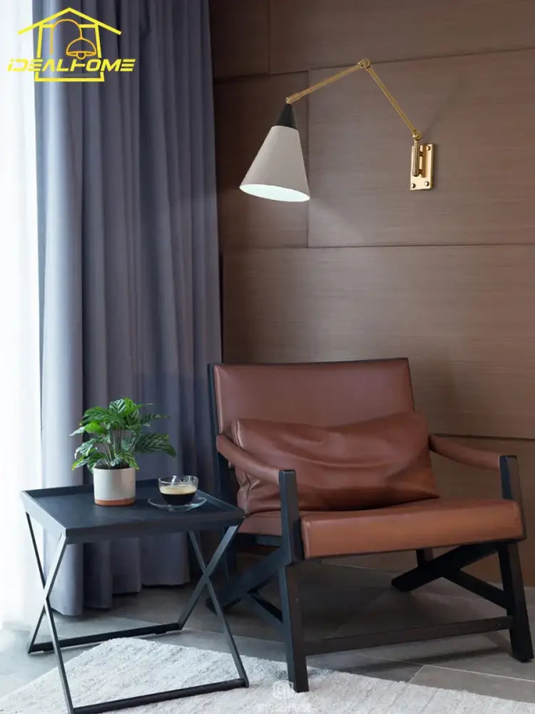 Brown leather armchair with black metal frame next to decorbites gold lustre brass swing arm wall lamp with white shade