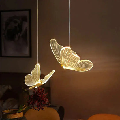Two illuminated gold metal butterfly pendant lights with glowing wings and delicate wireframe design for bedroom lighting