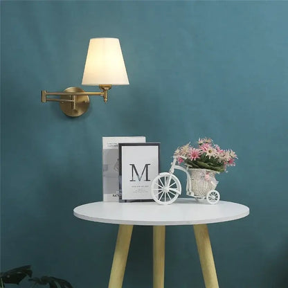White wicker bicycle planter with pink and white flowers beside gold pleated decorbites adjustable led wall lamp for bedroom reading