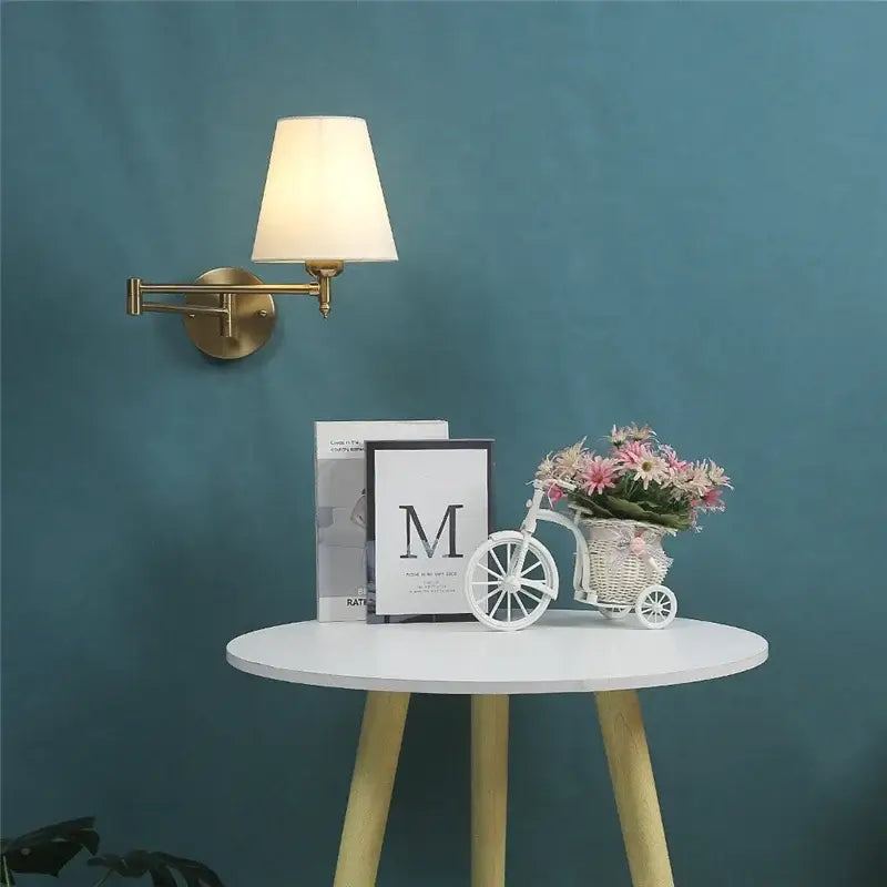 White wicker bicycle planter with pink and white flowers beside gold pleated decorbites adjustable led wall lamp for bedroom reading
