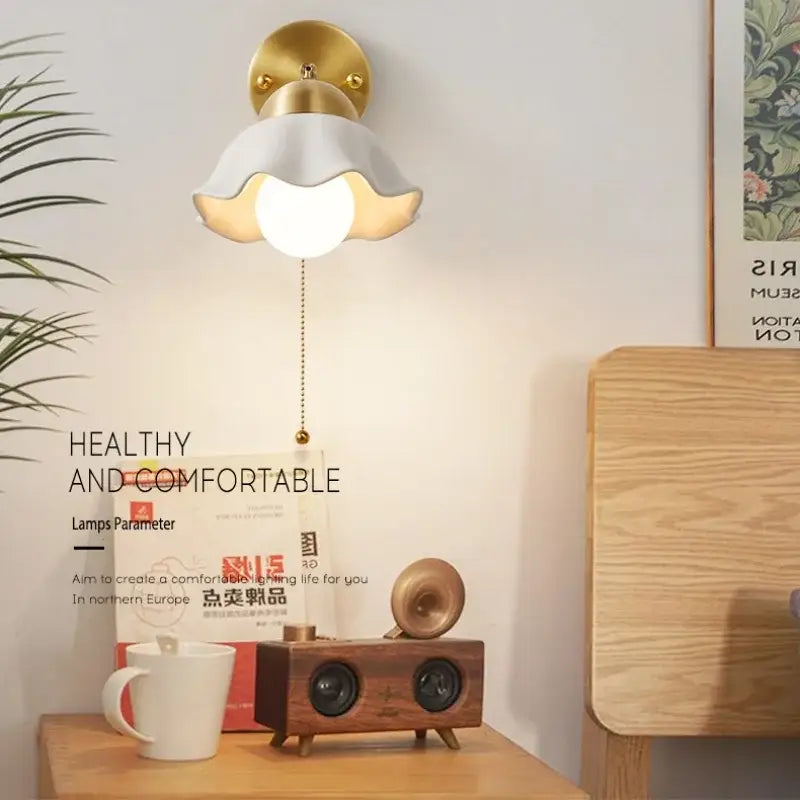 Gold finished wall light fixture with white fluted lampshade and illuminated bulb for bedroom use