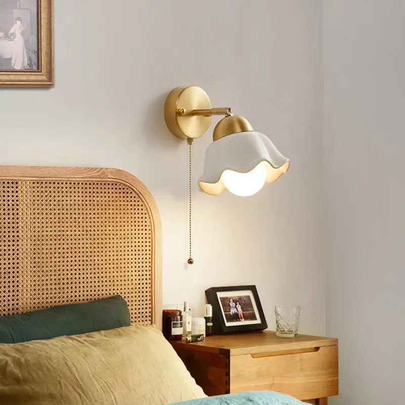 Gold-toned wall light fixture with a ruffled white glass shade and adjustable arm for bedroom pull chain lighting