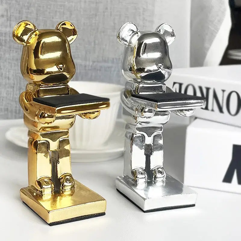 Two metallic gold and silver bear statue watch racks each holding a black tray for bedroom storage stand