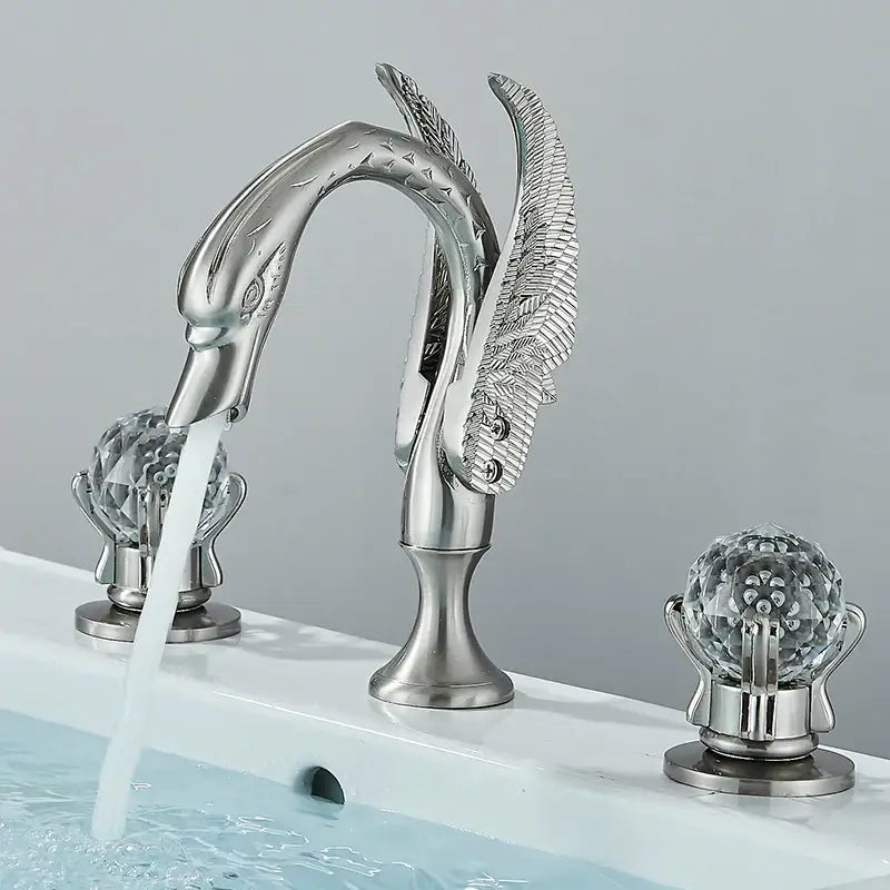 Silver swan-shaped bathroom faucet with ornate feather detailing and gold swan crystal globe handles by decorbites