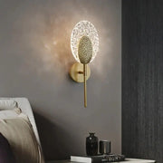 Gold-toned led wall lamp with textured oval glass diffuser and intricate metal backplate for indoor lighting