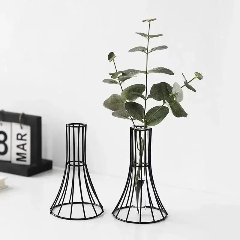 Black metal wireframe vase with flared base and slender neck holding green eucalyptus branches for modern desk decoration