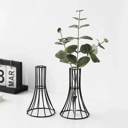 Black metal wireframe vase with flared base holding green eucalyptus branches for modern desk and metal flowers decor