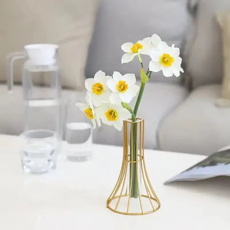 A slender gold vase metal wireframe holding white daffodils with yellow centers for modern desk decoration