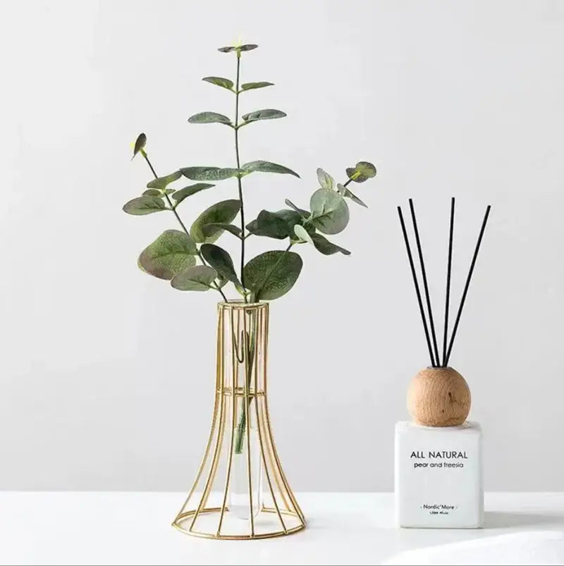 Gold wireframe vase holding green eucalyptus branches as modern desk decoration with metal flowers appeal