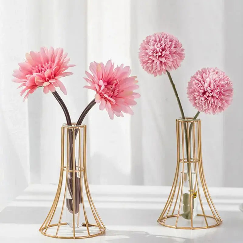 Gold wireframe vase with clear glass insert holding pink artificial metal flowers for modern desk decoration