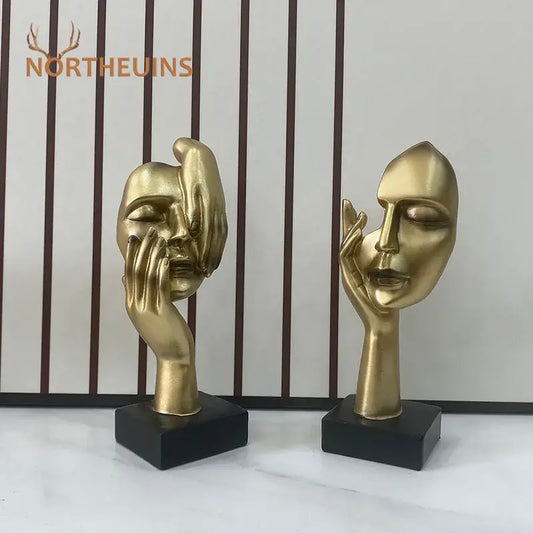 Golden abstract mask statue with hands framing features mounted on black bases for home office decor