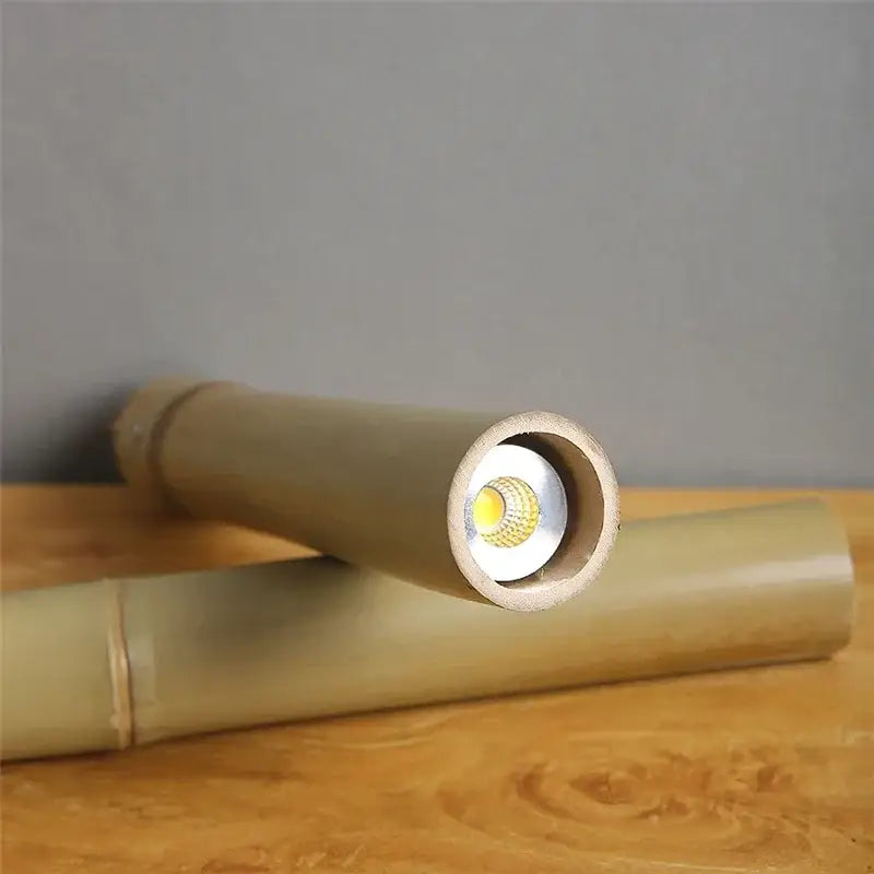 A sleek light brown bamboo tube pendant flashlight with a visible led bulb for adjustable dining room pendant lights