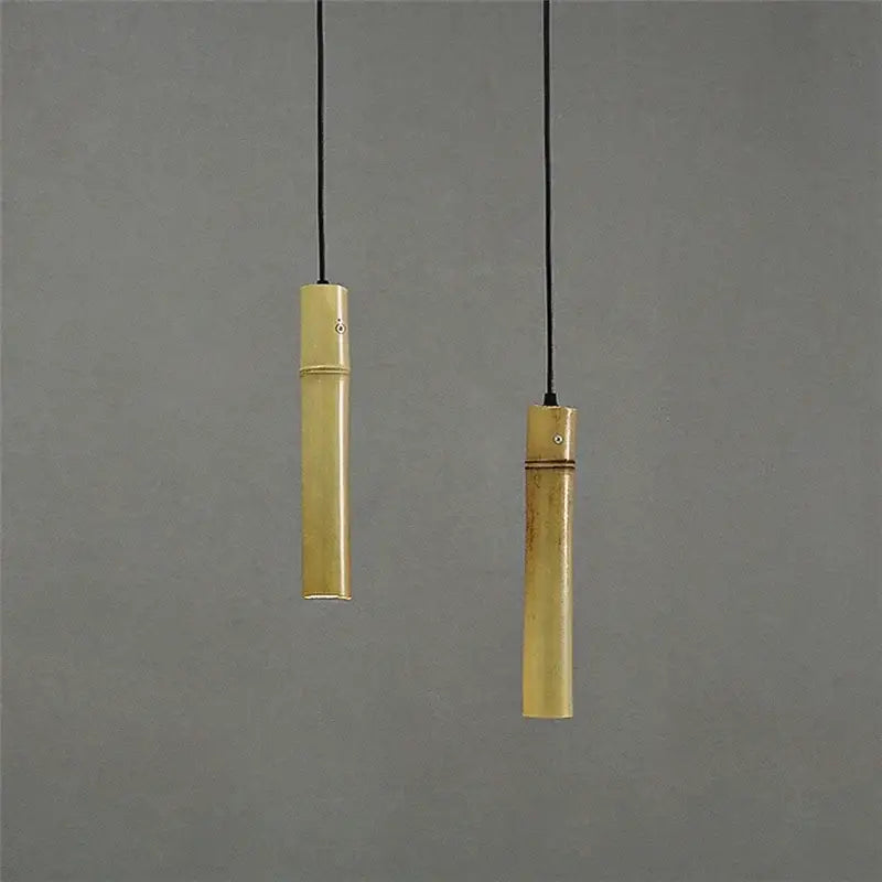 Two slender golden bamboo tube pendant lights with adjustable wire hang against a neutral gray backdrop for dining rooms
