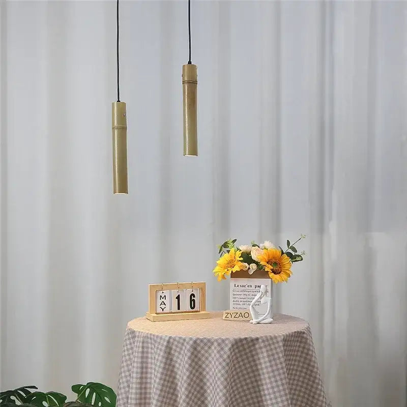 Two slender gold-finished bamboo tube pendant lights hang from black cords with adjustable wire for dining room use