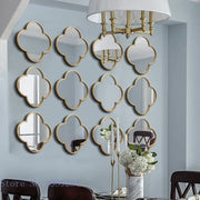 Set of twelve gold-framed geometric plum flower quatrefoil mirrors with golden border on light blue living room wall decor