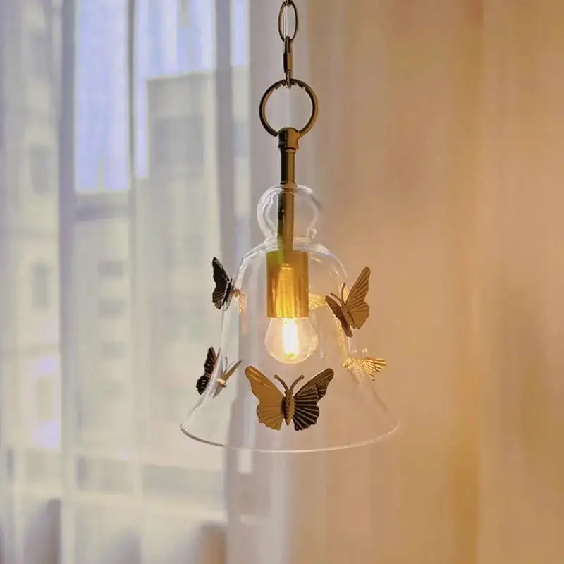 Golden butterfly bedhead glass pendant lamp featuring a clear bell-shaped glass pendant lamp with gold butterflies and brass chain