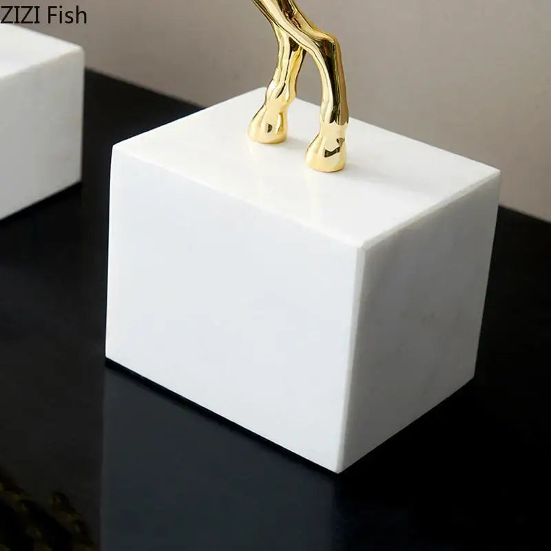 A sleek white marble base supporting a polished gold-colored decorbites deer antlers statue with white blossoms for living room decor