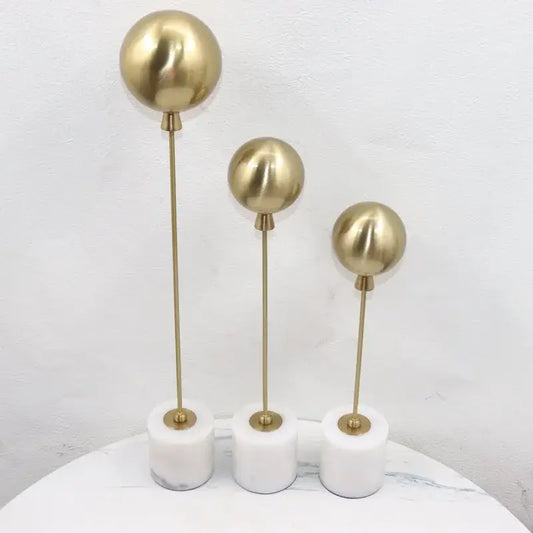 Set of three golden geometric balloon metal ball sculptures with gold-toned finish on white marble bases for living room decor