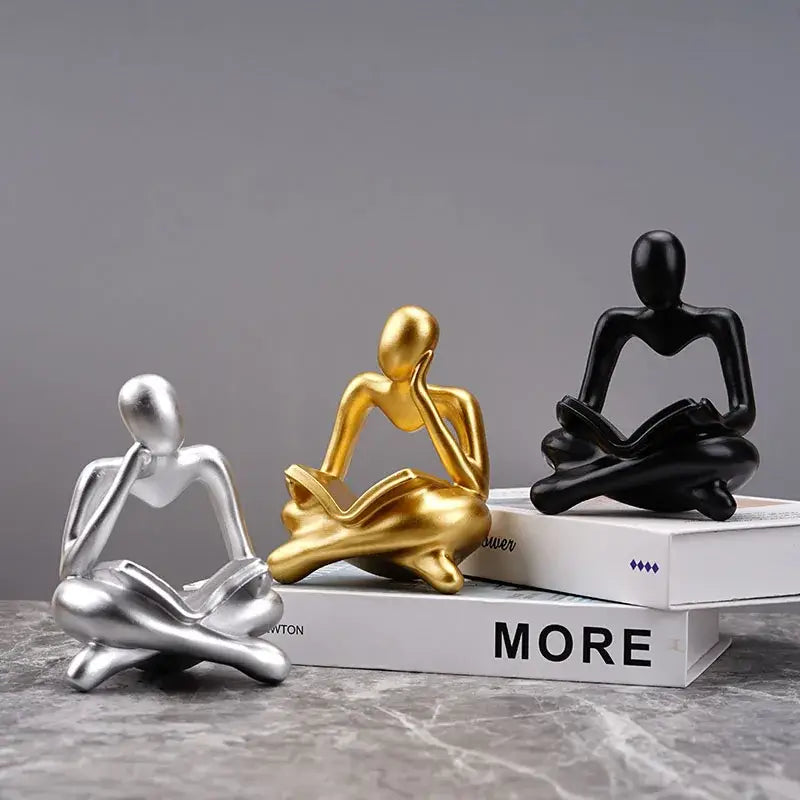 Three minimalist resin figurines in silver gold and black on stacked books for decorbites abstract thinker office decor