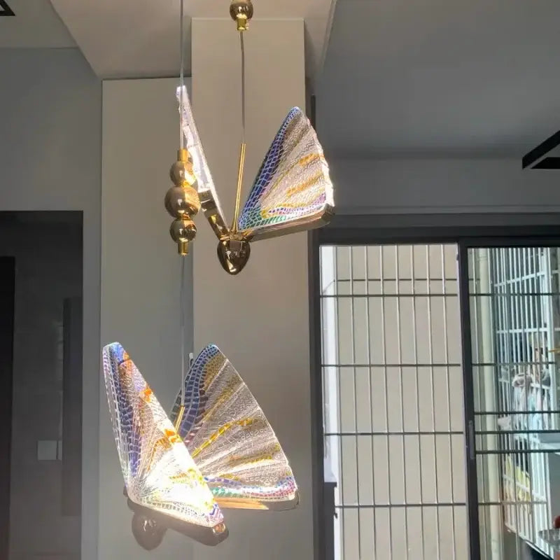 A pair of golden iridescent crystal butterfly pendant lamps with gold-toned frames and shimmering wings for bedroom lighting