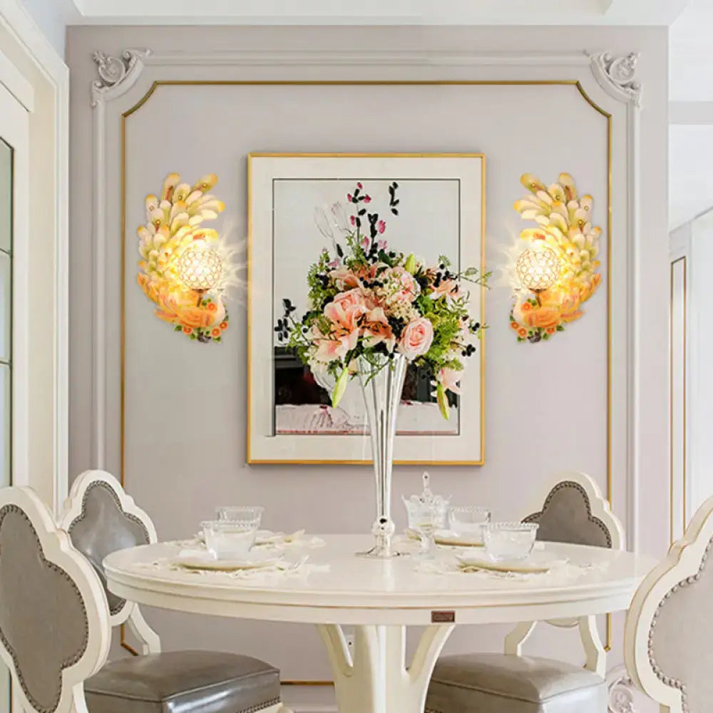 Golden peacock wall light with crystal shade yellow green features floral petal design flanking botanical artwork in dining room