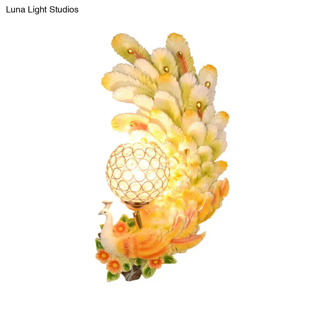 Golden peacock wall light with crystal shade featuring yellow green feathers and a glowing spherical bulb for living room use