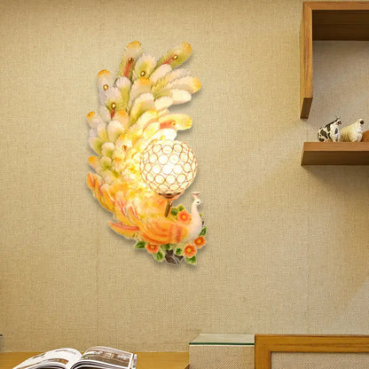 Golden peacock wall light with crystal shade featuring vibrant yellow green feathers and a glowing spherical lampshade