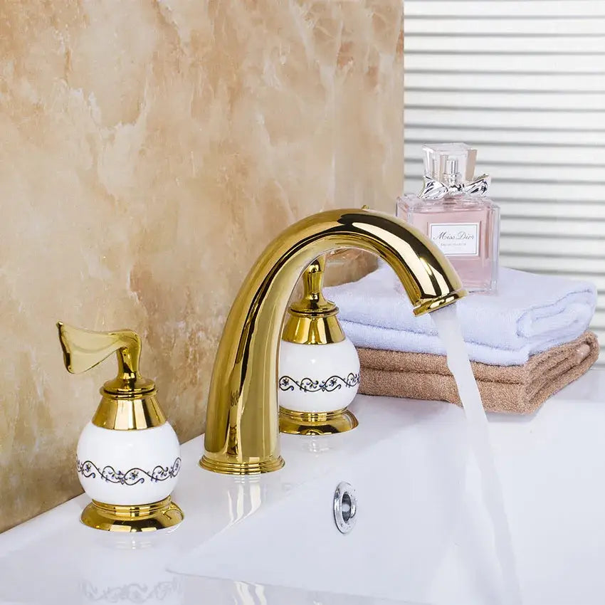 Golden plated bathroom faucet set with white ceramic handles and ornate black scrollwork by decorbites