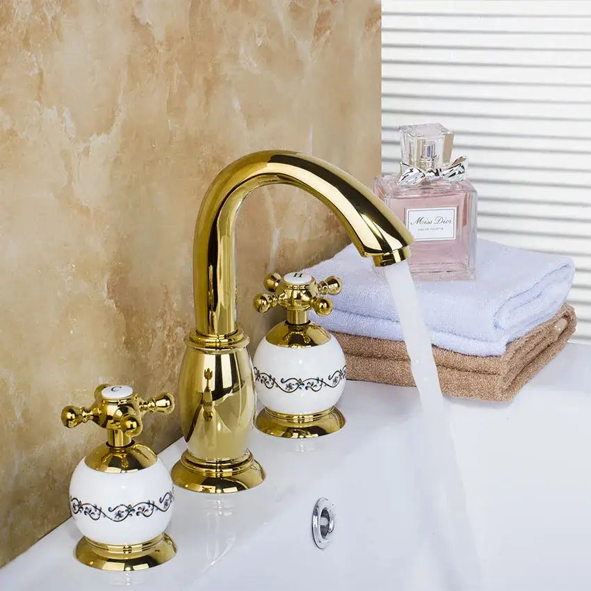 Golden plated bathroom faucet set with white ceramic handles featuring black floral detailing by decorbites