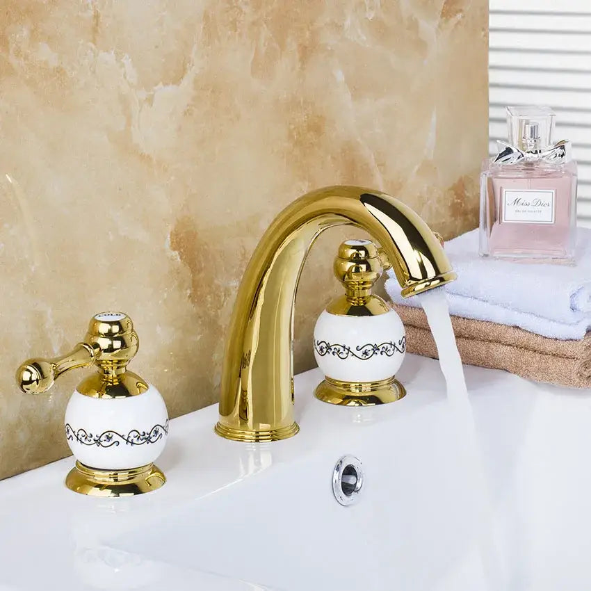 Golden plated bathroom faucet set with white ceramic handles featuring black ornate scrollwork by decorbites