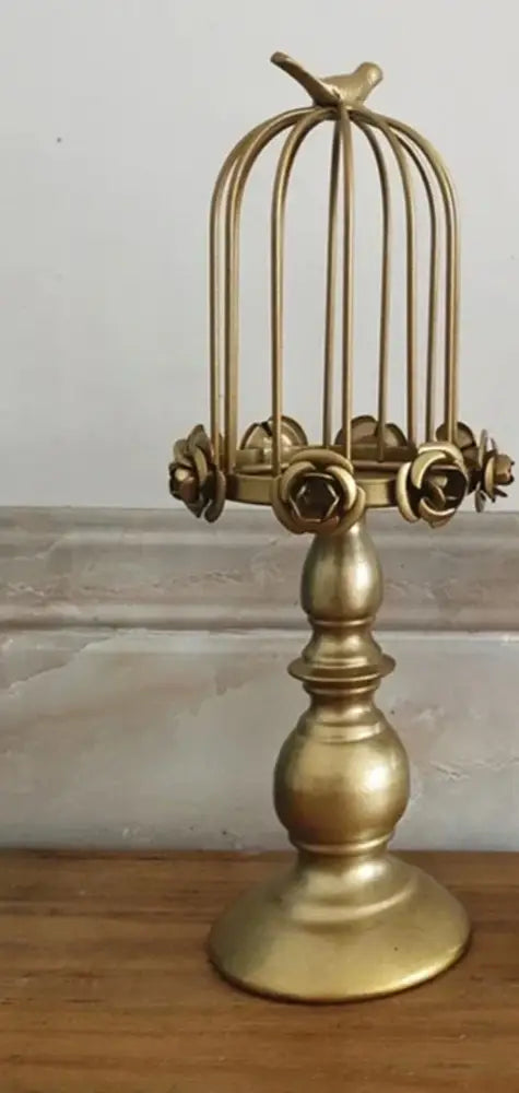 Golden metal birdcage style ornament with rose embellishments and small bird on top used as dining room candle holder