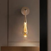 A sleek golden water droplets wall light with teardrop clear glass and illuminated filament bulb by decorbites