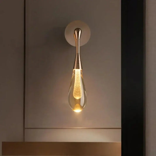 A sleek golden water droplets wall light with teardrop clear glass and illuminated filament bulb by decorbites