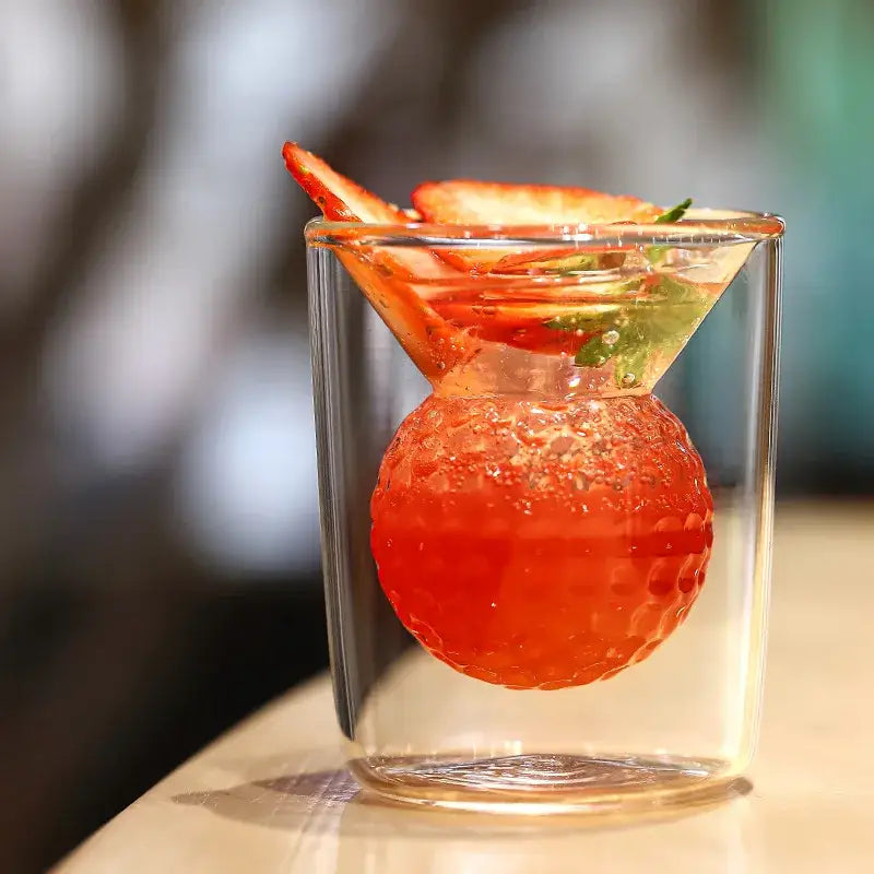 A vibrant red textured golf ball double tumbler made of thickened glass with strawberry drink and mint garnish decorbites golf ball