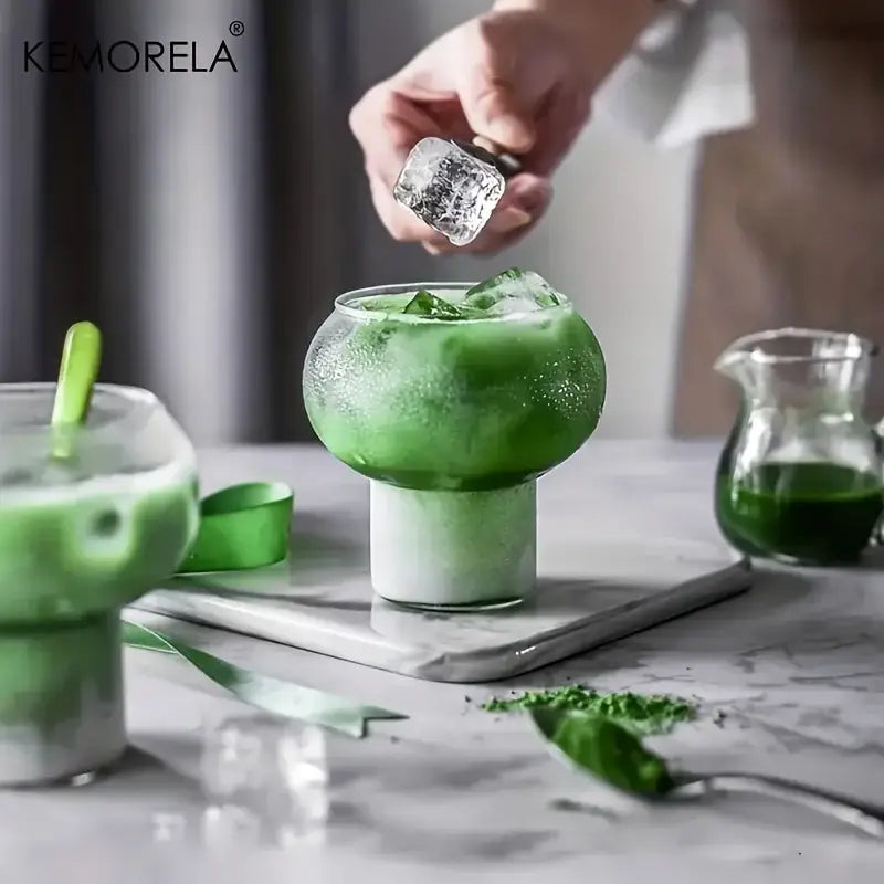 A sleek gourd shaped glass cup with frosted green upper section and clear base filled with vibrant matcha drink