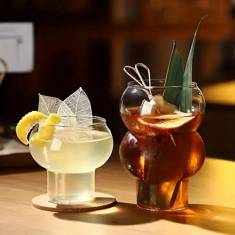 Two uniquely shaped gourd shaped glass cups in a glass cup set with wooden handles holding yellow and amber drinks