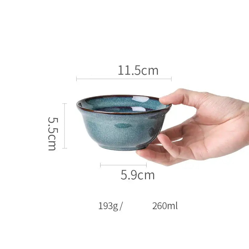 A hand holds a beautiful blue ceramic bowl with deep teal glaze and gold rim dinnerware dish for dining room use