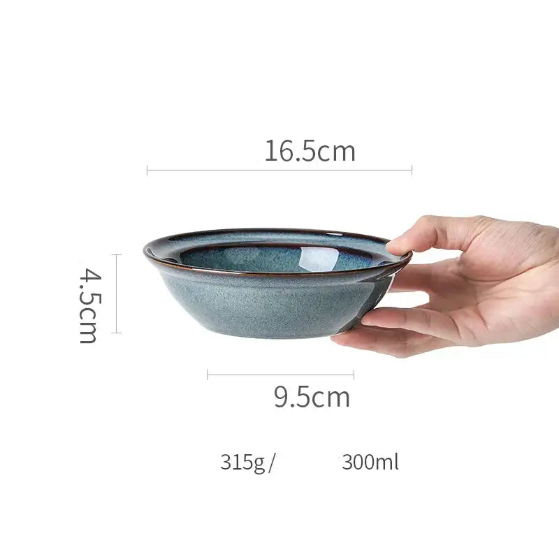 A hand holds a beautiful blue ceramic bowl with deep glaze and dark rim dinnerware dish for dining room use