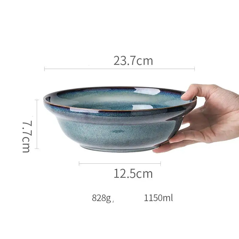 A hand holds a beautiful blue ceramic bowl with gradient glaze and gold rim dinnerware dish for dining room use