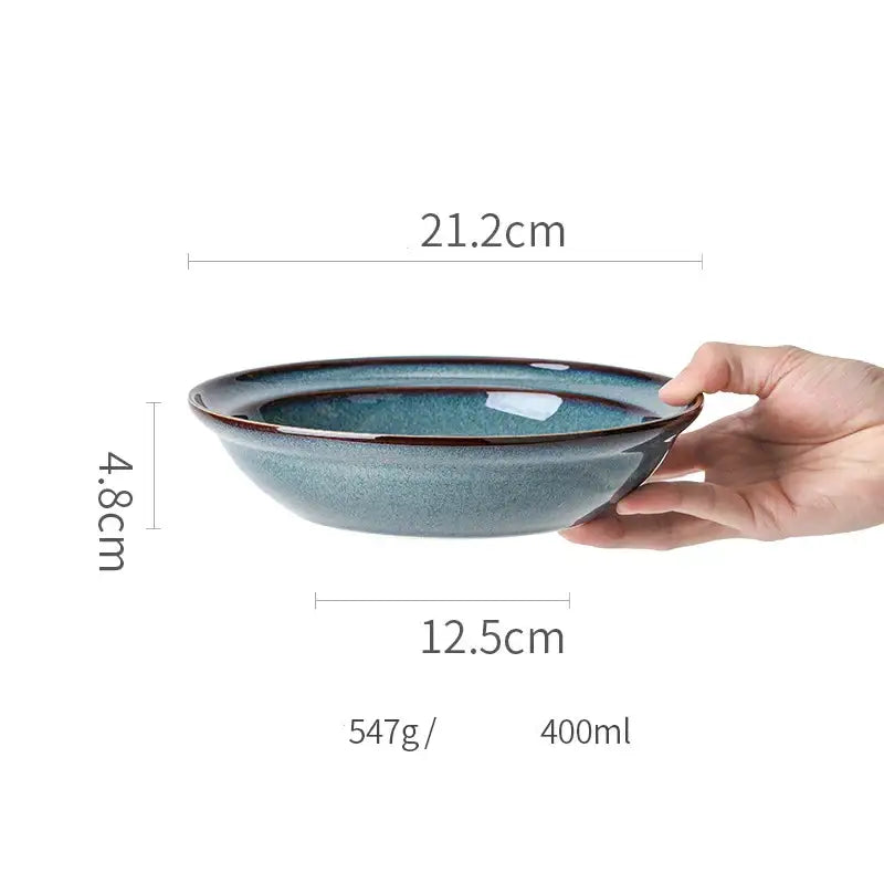 A hand holds a beautiful blue ceramic bowl with a gold rim dinnerware dish measuring 21.2cm diameter