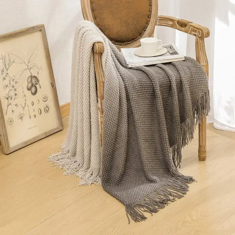 A cozy gray knit blanket with textured fabric and fringed edges draped over a wooden chair featuring decorbites gradient pineapple grid