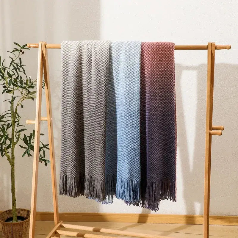 Three knit blankets in gray blue and purple with matching fringe hang on a wooden rack decorbites gradient pineapple grid