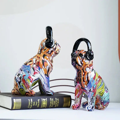 Two vibrant graffiti resin bulldog headphone figurines wearing black headphones sit side by side on a book
