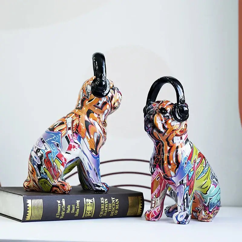 Two vibrant graffiti resin bulldog headphone figurines wearing black headphones sit side by side on a book